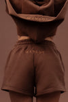 A model shown from behind wearing a matching brown cropped hoodie and shorts set with &
