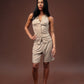 A woman modeling a light beige sleeveless button-front romper with matching shorts, standing against a solid dark brown studio backdrop.
